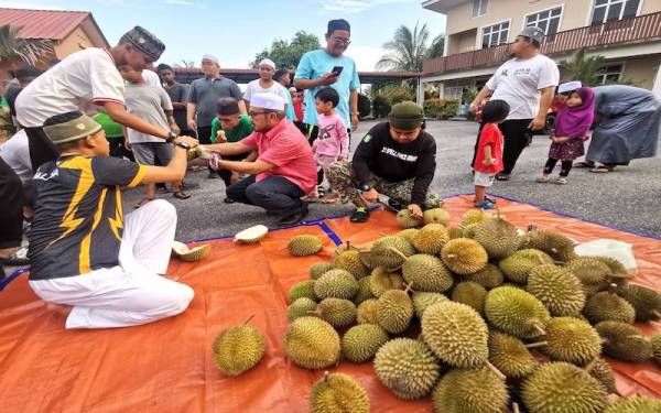 Zulkifli (berbaju merah jambu) menghulurkan buah durian yang telah dikupas kepada pelajar tahfiz Madrasah Khoirul Uloom.