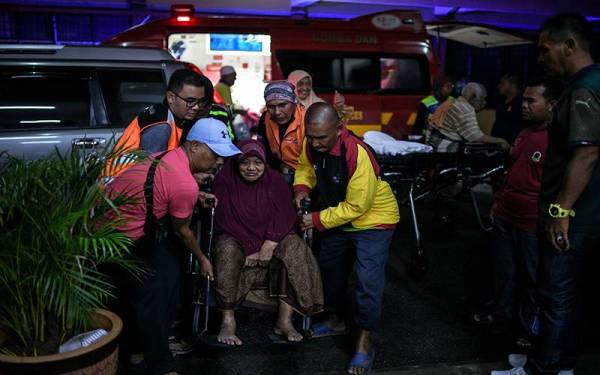 Penduduk kampung bersama Jabatan Kebajikan Masyarakat (JKM) membantu memindahkan warga emas yang diselamatkan oleh anggota Bomba selepas rumah mereka dilanda banjir di sini petang Isnin. - Foto Bernama
