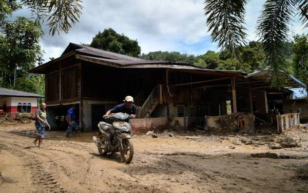 Penduduk setempat menolak motosikal yang rosak selepas dilanda banjir petang Isnin. - Foto Bernama