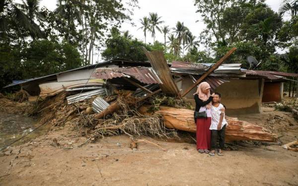 Mangsa banjir, Norhayati Ismail,36, bersama Muhammad Firash Mohd Shahrim, 9, di hadapan rumah mereka yang ditimbuni kayu balak setelah dibawa arus deras dalam kejadian banjir. - Foto Bernama