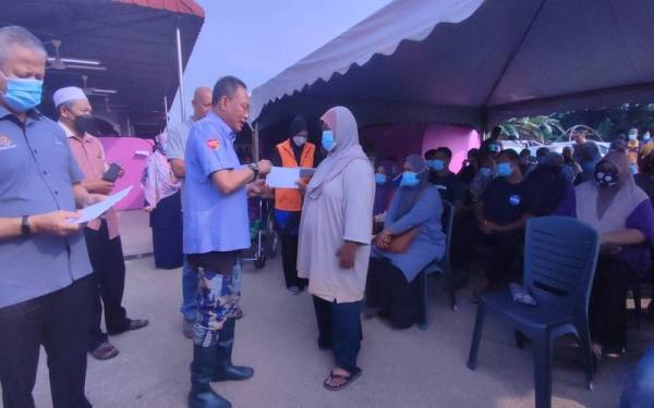 Awang (tengah) menyerahkan sumbangan kepada mangsa banjir pada Program Penyerahan Sumbangan CSR kepada mangsa banjir di PPS Surau An-Nur pada Jumaat.