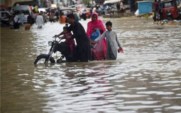 Sebuah keluarga melalui jalan yang dinaiki air selepas hujan lebat di Karachi, Pakistan. - Foto AFP