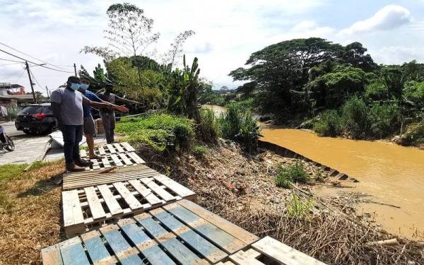 Kamarul Azman (kiri) menunjukkan lokasi hakisan tanah di Sungai Linggi yang terletak berhampiran dengan rumah penduduk.