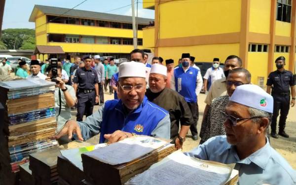 Idris (kiri) meninjau kerosakan bahan bacaan akibat banjir dan kepala air di SMA Arab Yayasan Khairiah, Kupang, Baling pada Ahad.