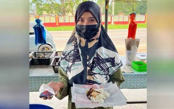 Zuraida menunjukkan nasi lemak berharga RM1 sebungkus yang dijual di kedainya.