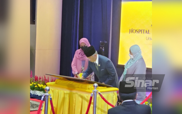 Al-Sultan Abdullah sambil diperhatikan Menteri Pengajian Tinggi, Datuk Seri Dr Noraini Ahmad (kiri) dan Dr Roziah (kanan) menandatangani plak perasmian pada Majlis Perasmian Hospital Al Sultan Abdullah UiTM di Puncak Alam pada Sabtu.