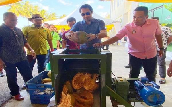 Wan Ahmad Fayhsal (dua dari kanan) mencuba sendiri mesin mengupas kelapa semasa lawatannya ke Kilang Projek D'Raja Kelantan di Telong, Bachok pada Jumaat