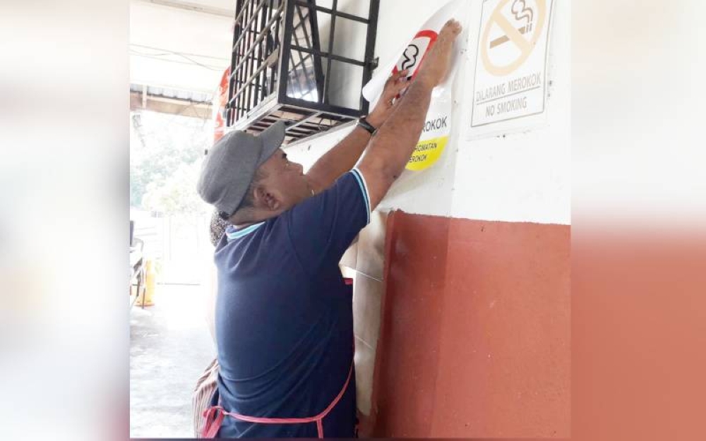 Peniaga kedai makan, Husin Omar, 43, menampal pelekat dilarang merokok pada dinding kedai di pekan Lubok Cina, dekat Masjid Tanah pada Khamis.