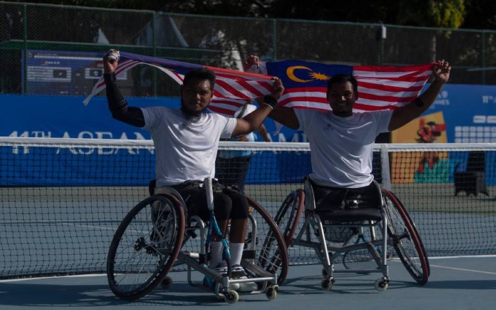 Atlet Paralimpik Negara Abu Samah Borhan (kiri) dan Mohammad Yusshazwan (kanan) mengibarkan jalur gemilang selepas memenangi perlawanan menentang Pemain Tenis Para Indonesia Kevin Sanjaya dan Agus Fitriadi dalam acara beregu lelaki tenis berkerusi roda pada Sukan Para ASEAN 2022 Solo di Lapangan Tenis Manahan, pada Jumaat. - Foto Bernama 