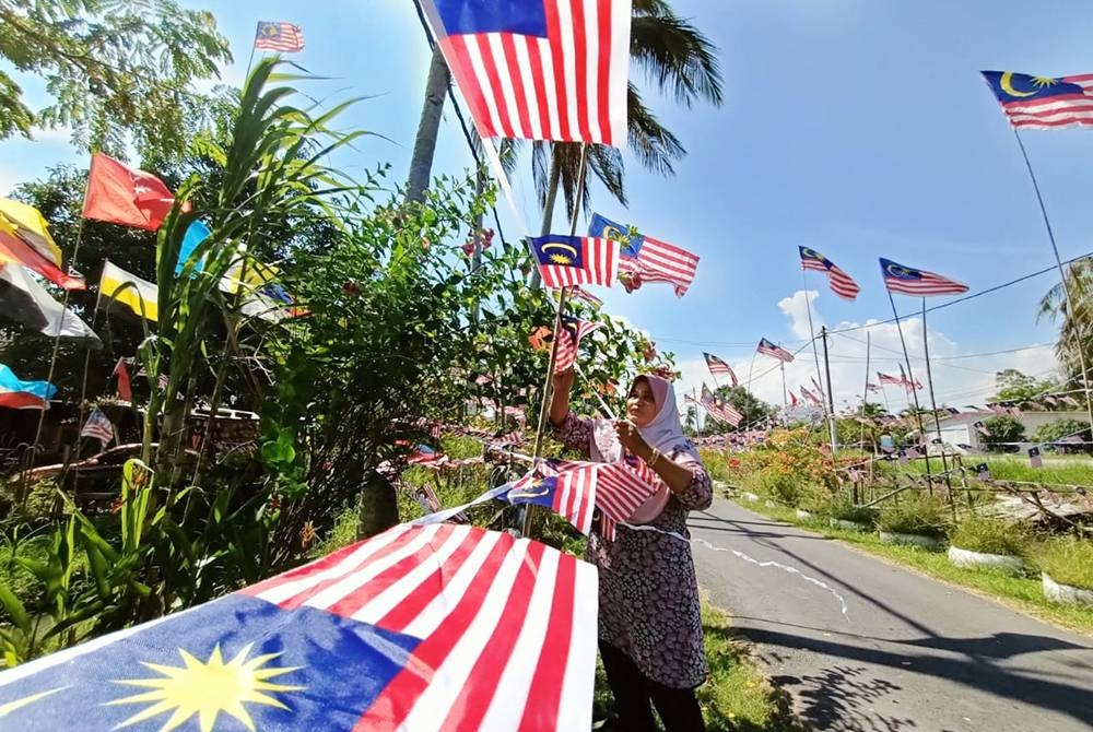 Norhayawati sedang memasang bendera kecil yang dibelinya di hadapan rumah mereka di Kampung Batu 8 Jalan Alor Setar -Sungai Petani di sini pada Ahad.