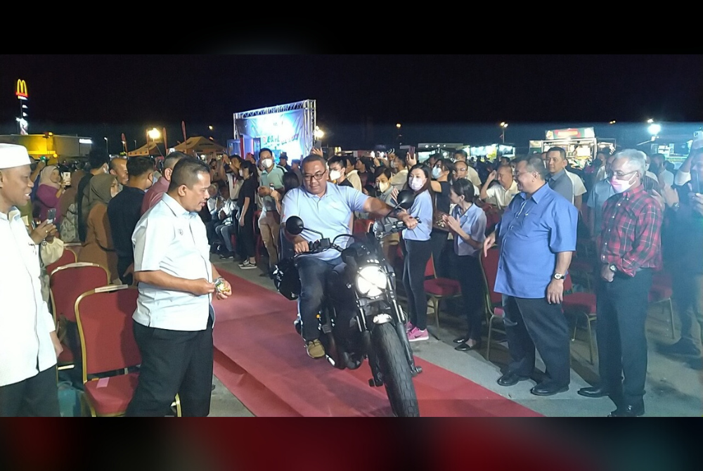 Muhammad Sanusi melakukan gimik menunggang motosikal menuju ke pentas utama semasa Majlis Pelancaran dan Menandatangani Perjanjian Projek Litar Lumba PKB Open Road SP Circuit Sungai Petani di Dataran Amanjaya Mall di sini, pada Isnin.