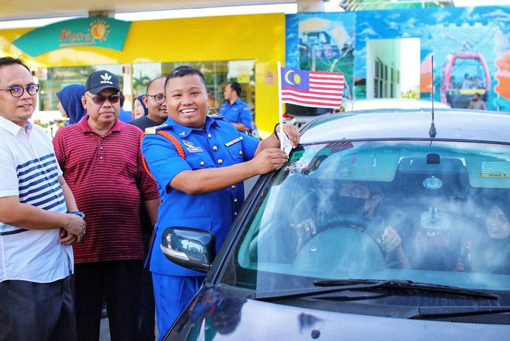 Amirul Syahir (kanan) melekatkan bendera pada kereta milik pengunjung stesen minyak di Kuala Kedah untuk menyemarakkan bulan Kemerdekaan.