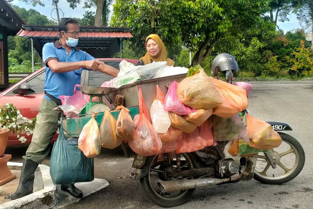 Ahmad Diah (kiri) melayan seorang pelanggan yang membeli barang jualannya di Kampung Pengkalan Batu.