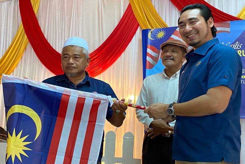 Wan Ahmad Fayhsal (kanan) menyampaikan Jalur Gemilang pada Majlis Ramah Mesra Merdeka Keluarga Rukun Tetangga Pengkalan Chepa, Kota Bharu pada Isnin.