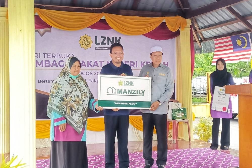 Kamariah (kiri) menerima replika penyerahan bantuan rumah daripada Azizul Rusmadi di Majlis Penyerahan Bantuan Rumah di Masjid Al-Falah, Sungai Tiang pada Selasa.