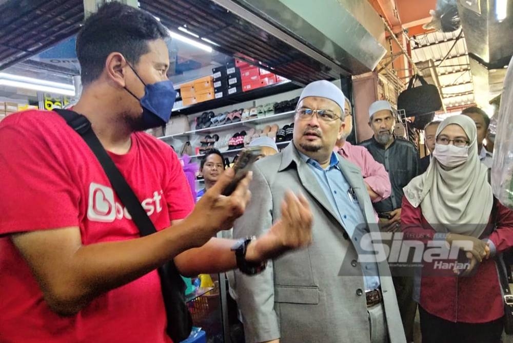 Mohamed Fadzli (tengah) mendengar penerangan daripada seorang peniaga mengenai kaedah penggunaan pembayaran tanpa tunai.