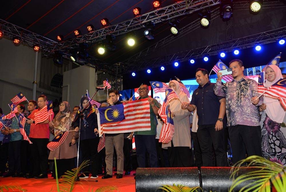 Muhammad Sanusi (tengah) mengibarkan bendera Jalur Gemilang pada Majlis Ambang Merdeka Hari Kebangsaan ke-65 di Dataran Pekan Rabu, pada Selasa.