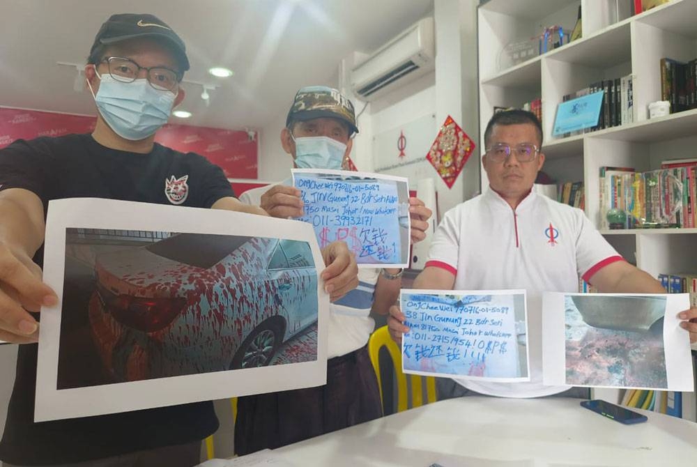 Queck Hui (tengah) menunjukkan nota ditinggalkan suspek manakala anaknya menunjukkan gambar kereta disimbah cat merah di Pejabat ADUN Johor Jaya, Taman Johor Jaya< Pasir Gudang, pada Jumaat.