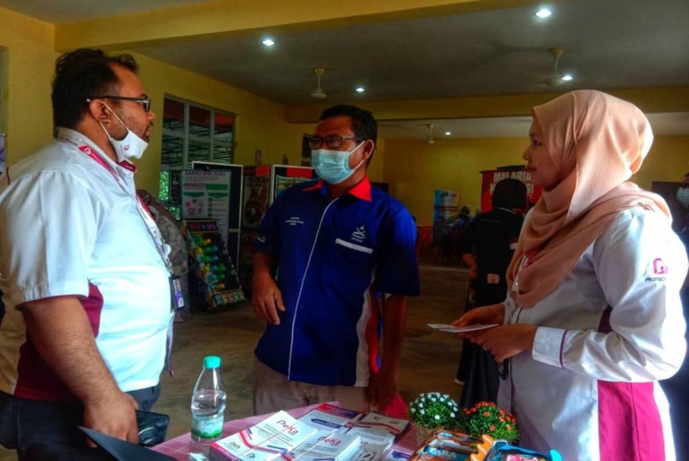 Mohd Fadzrel (kiri) bersama petugas ProtectHealth (kanan) memberikan penerangan kepada penduduk yang hadir dalam program tersebut.