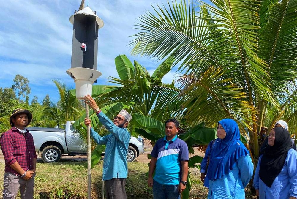 Nik Muhammad Zawawi (empat dari kanan) memasang perangkap kumbang sebagai gimik perasmian semasa mengadakan lawatan ke projek tanaman kelapa di Gong Tengah, Pasir Puteh pada Sabtu.