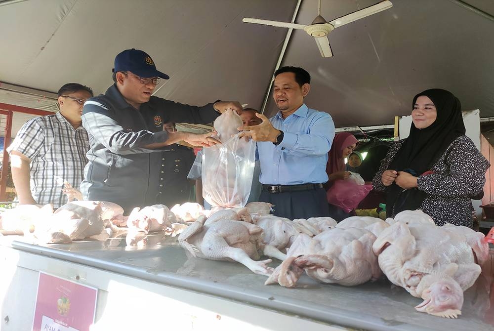 Azman (dua dari kiri) bersama Pengarah KPDNHEP Terengganu, Saharuddin Mohd Kia (tengah) membantu seorang pelanggan membeli ayam ketika meninjau PJMKM di Kampung Duyong, di sini pada Ahad.