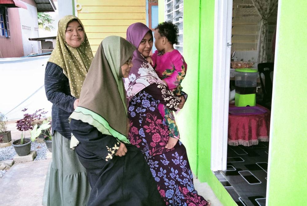 Rahimah (tengah) bersama anak, Norhayati Mohamad Zain, 41 (kanan) dan menantu, Noatiqi Rasidi, 37 (kiri) melangkah masuk ke rumah mereka selepas Majlis Penyerahan Rumah Dhuafat di Kampung Kutan Tengah pada Khamis.