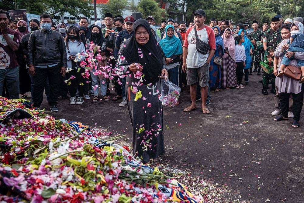 Seorang wanita menabur bunga di pusara mangsa dalam kejadian rempuhan di Stadium Kanjuruhan di Malang, Jawa Timur pada akhir minggu lalu. - Foto: AFP