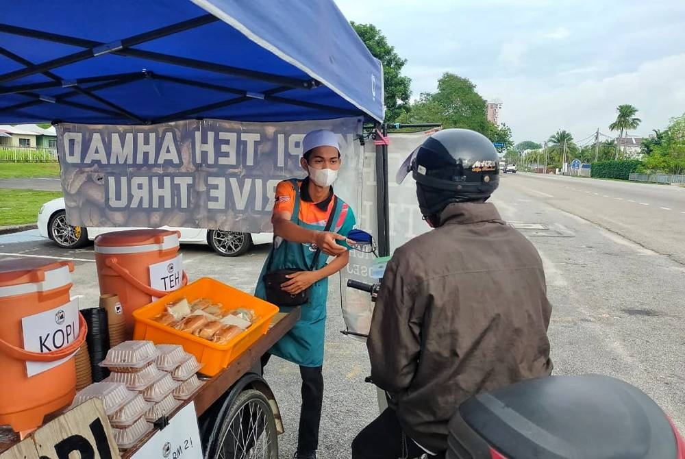 Ahmad Usamah (kiri) ketika melayan pelanggannya membeli minuman secara pandu lalu.