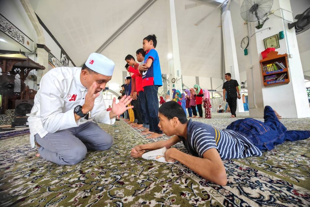 Ahmad Idham menunjukkan cara solat kepada Luqman Hakim yang menghidap cerebral palsy.