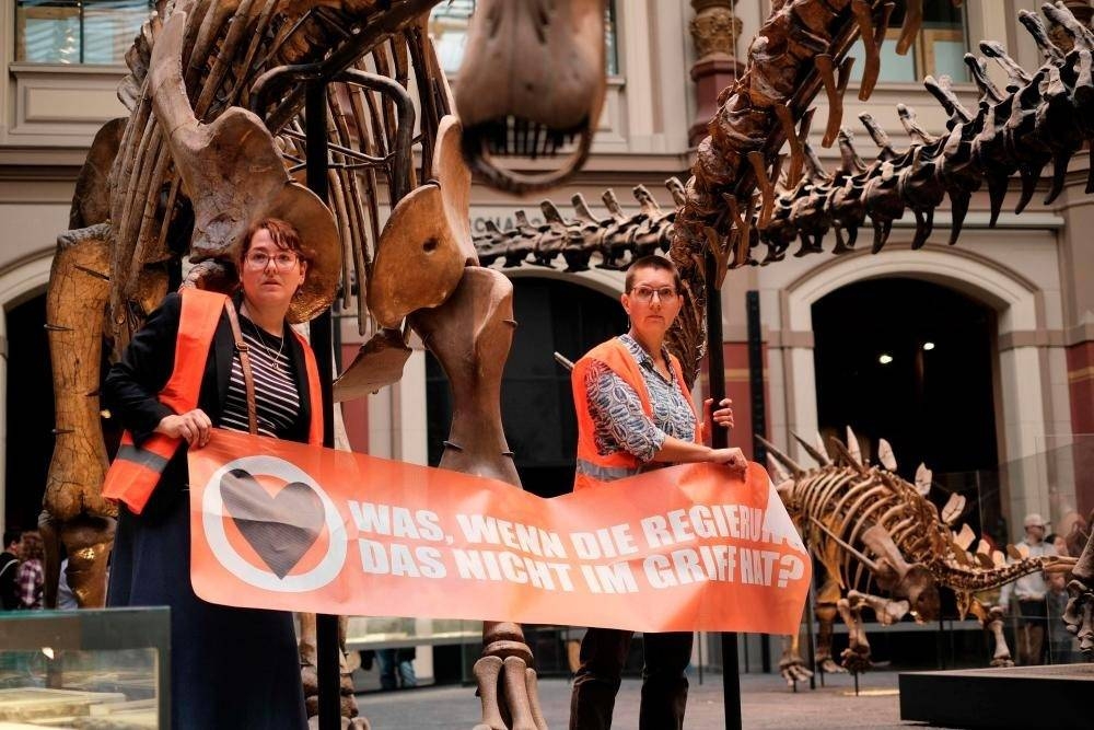 Dua aktivis bertindak mengamkan diri masing-masing pada struktur logam yang menyokong rangka tulang dinaosaur di Muzium Semula Jadi di Berlin pada Ahad. - Foto AFP