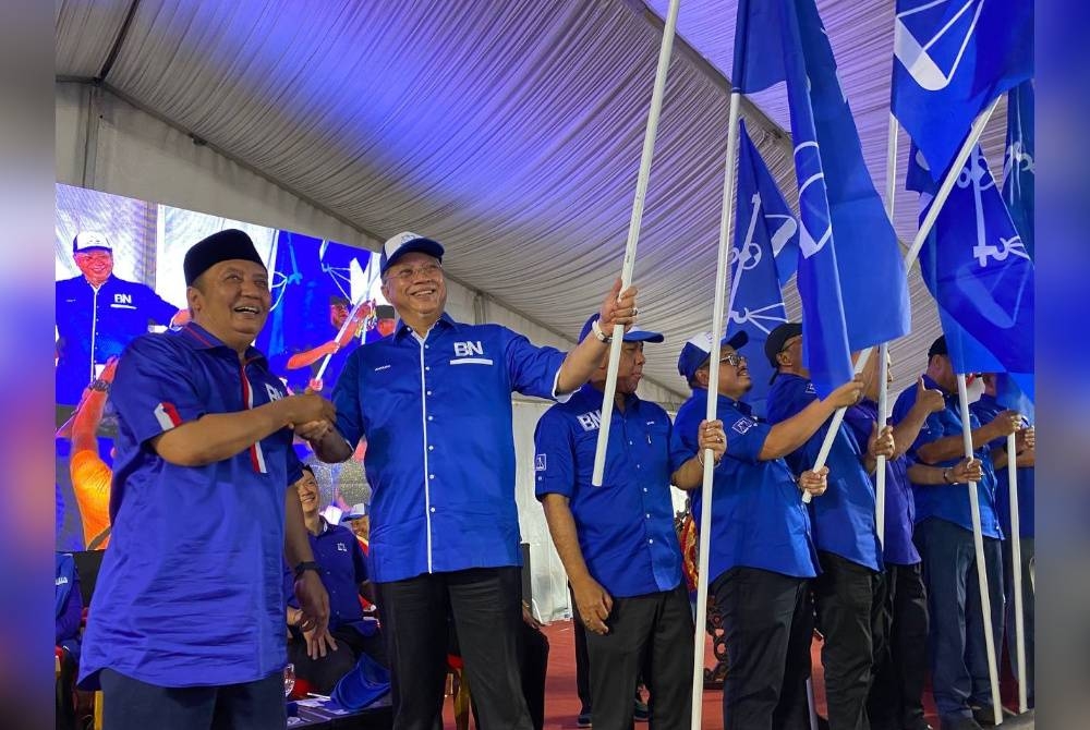 Ahmad Jazlan (kiri) menyerahkan bendera BN kepada Annuar semasa majlis pelancaran Jentera BN di Labok, Machang pada Isnin.