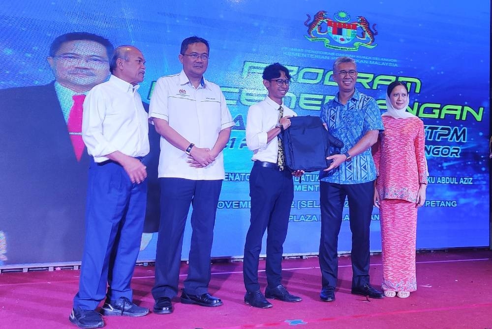 Tengku Zafrul (dua dari kanan) sambil diiringi Pegawai Pendidikan Daerah Kuala Selangor, Mohd Azwan Mohd Nawawi (dua dari kiri) menyampaikan sumbangan kepada penerima pada Program Kecemerlangan Pelajar SPM dan STPM Parlimen Kuala Selangor di One Plaza di Kuala Selangor pada Selasa.