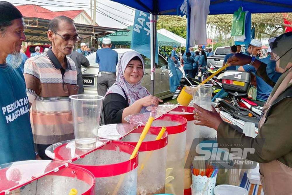 Asiah (kanan) melayan pelanggan dan penyokong yang membeli di gerainya pada Pusat Penamaan Calon Kompleks Pentadbiran Daerah Perak Tengah di Kampung Gajah.