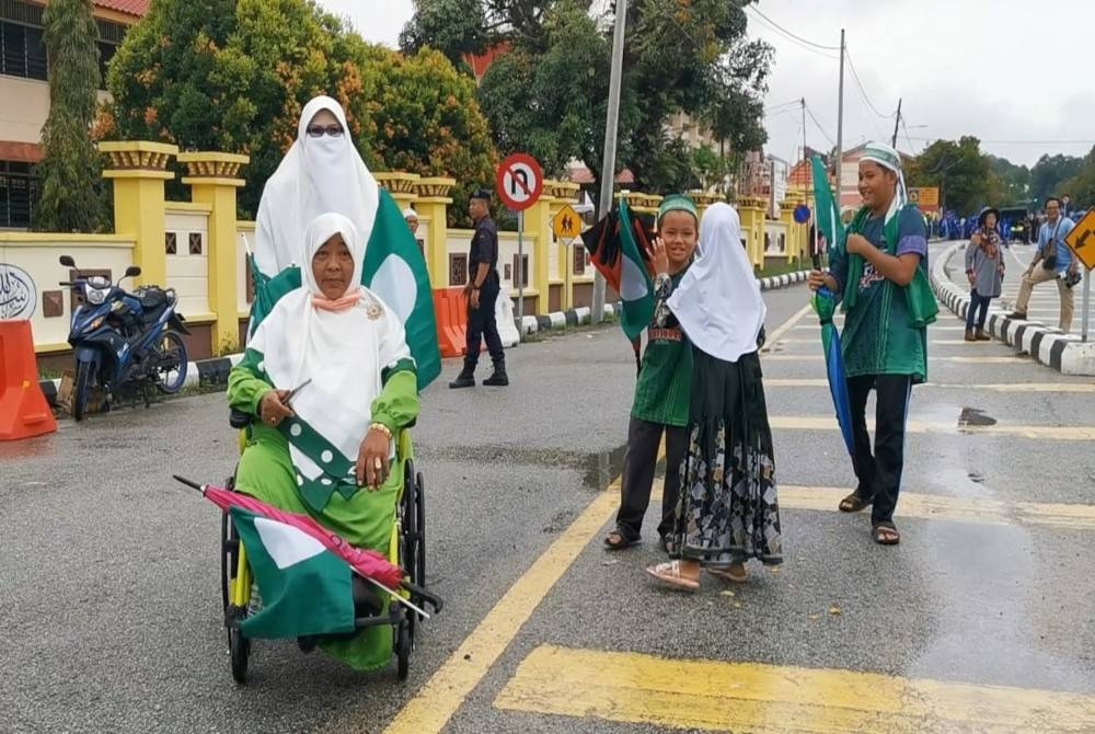 Zamidah (berkerusi roda) dibantu rakannya, Nor Zalida di hadapan Pejabat Daerah dan Tanah Marang pada Sabtu.