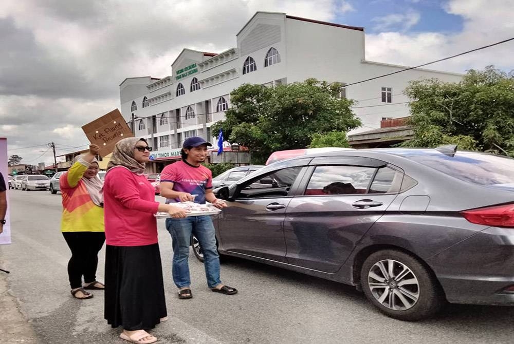 Aiman (kanan) mengagihkan kek pisang kepada pemandu di Jalan Pintu Geng pada Rabu.