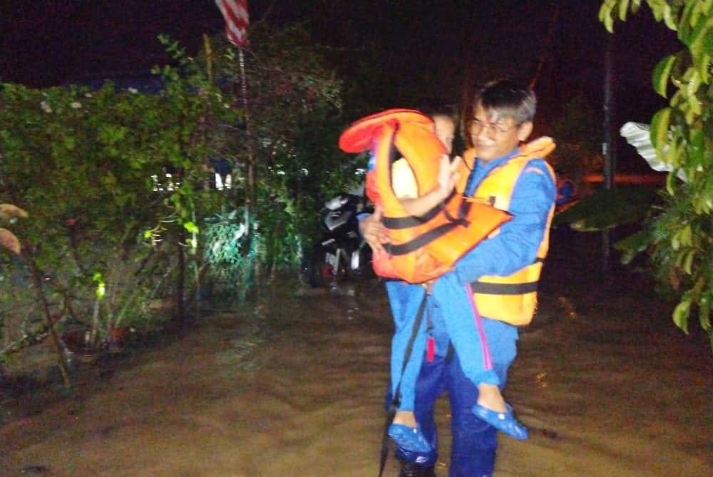 Anggota APM menyelamatkan seorang kanak-kanak ke tempat selamat selepas kediaman mereka dinaiki air.