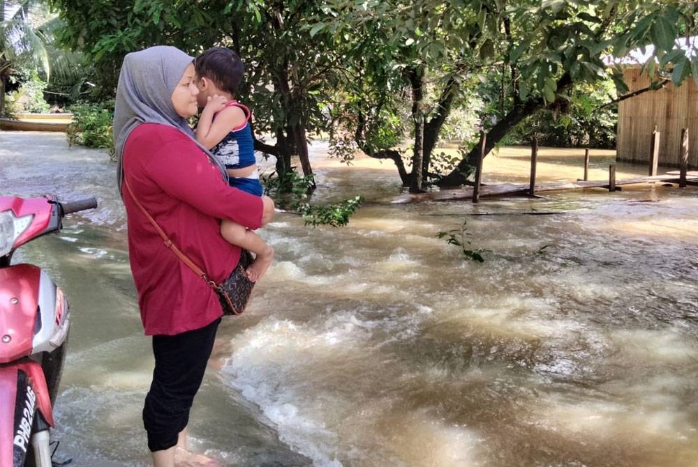 Wan Rohaya melihat keadaan rumahnya yang ditenggelami air akibat hujan lebat pada Jumaat.