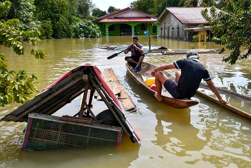 Penduduk menggunakan sampan untuk meninjau keadaan rumah mereka yang ditenggelami banjir ketika tinjauan di Kampung Tersang, Rantau Panjang pada Isnin. - Foto Bernama