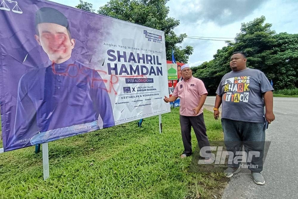 Nizam (kiri) dan Mohd Ghazali (dua,kiri) menunjukkan gambar calon BN Parlimen Alor Gajah yang telah dirosakkan di Persimpangan Ayer Pasir, di sini, pada Jumaat.