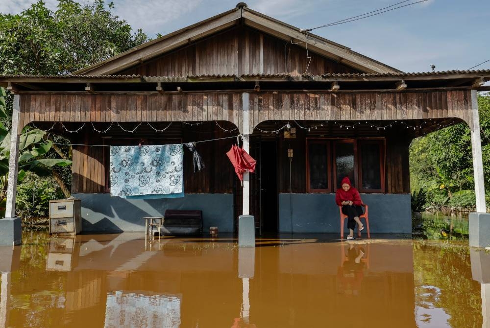 Seorang wanita melihat telefon pintar di halaman rumahnya yang dilanda banjir di Kampung Johan Setia pada Jumaat. - Gambar hiasan