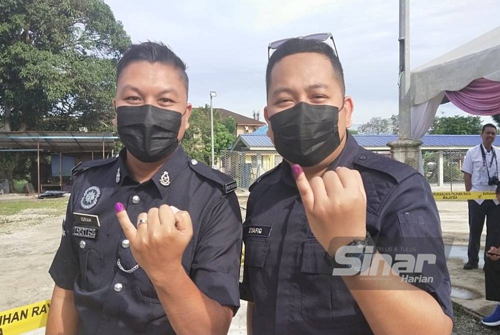 Mohd Shafiq (kanan) dan Mohd Jamilul Ikram menunjukkan kesan dakwat pada jari kelingking selepas selesai mengundi di pusat pengundian awal di IPD Rompin di sini pada Sabtu.