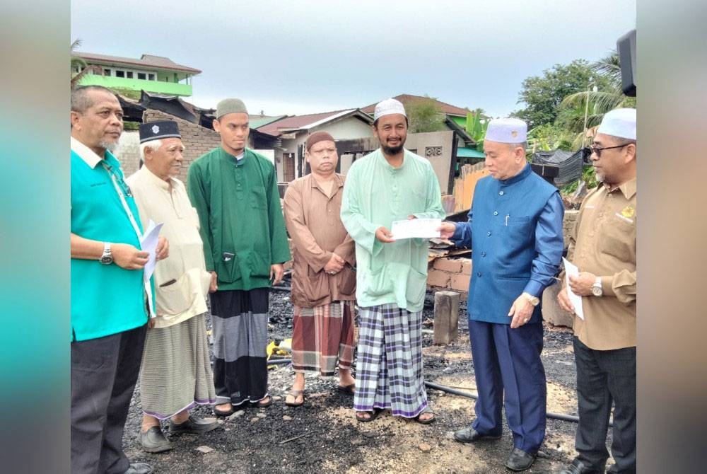 Azami (dua dari kanan) menyampaikan sumbangan kepada Ahmad Shairazi selepas meninjau keadaan rumah yang terbakar di Kampung Terusan Limbat pada Ahad.