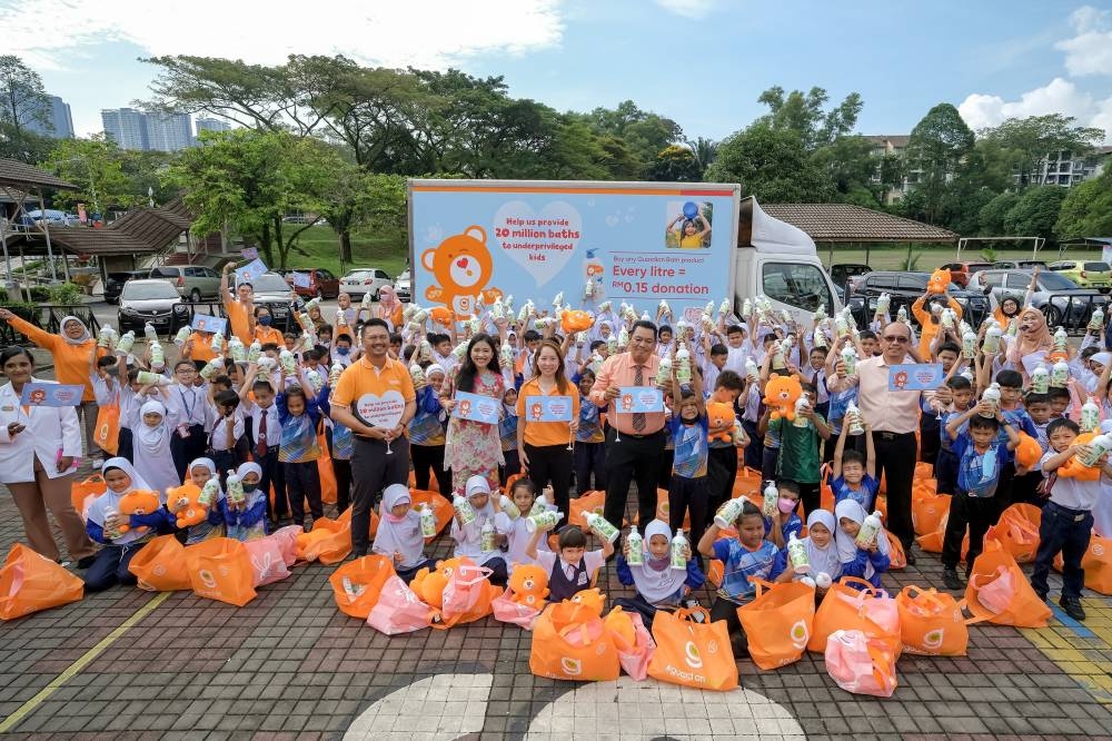 Sebahagian kanak-kanak sekolah rendah bersama pasukan Guardian menunjukkan botol mandian yang diterima.