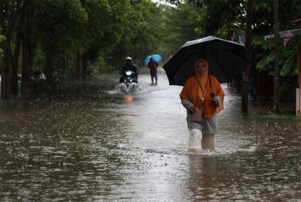 Seorang wanita meredah air yang melimpahi jalan ekoran hujan lebat berterusan semasa tinjauan di Kampung Gong Tok Nasek, Kuala Terengganu pada Jumaat. - Foto Bernama