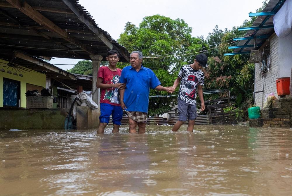 Suhaimi dibantu cucunya meredah air untuk mendaftar masuk ke PPS di Sekolah Kebangsaan Kubang Kual ekoran rumah mereka ditenggelam air hujan lebat berterusan sejak tiga hari lalu semasa tinjauan di Kampung Kubang Kual di sini. - Foto Bernama