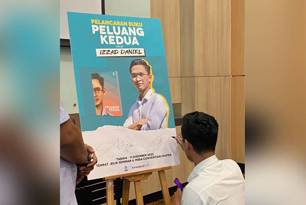 Muhammad Izzad menurunkan tandatangan pada poster perasmian ketika Majlis Pelancaran Buku Peluang Kedua.