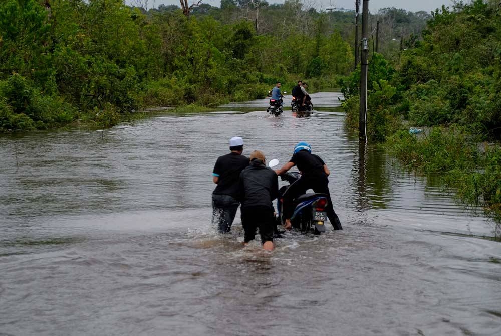 Beberapa penunggang motosikal meredah banjir yang menenggelamkan sebahagian jalan di Kampung Air Hitam, pada Selasa. - Foto Bernama