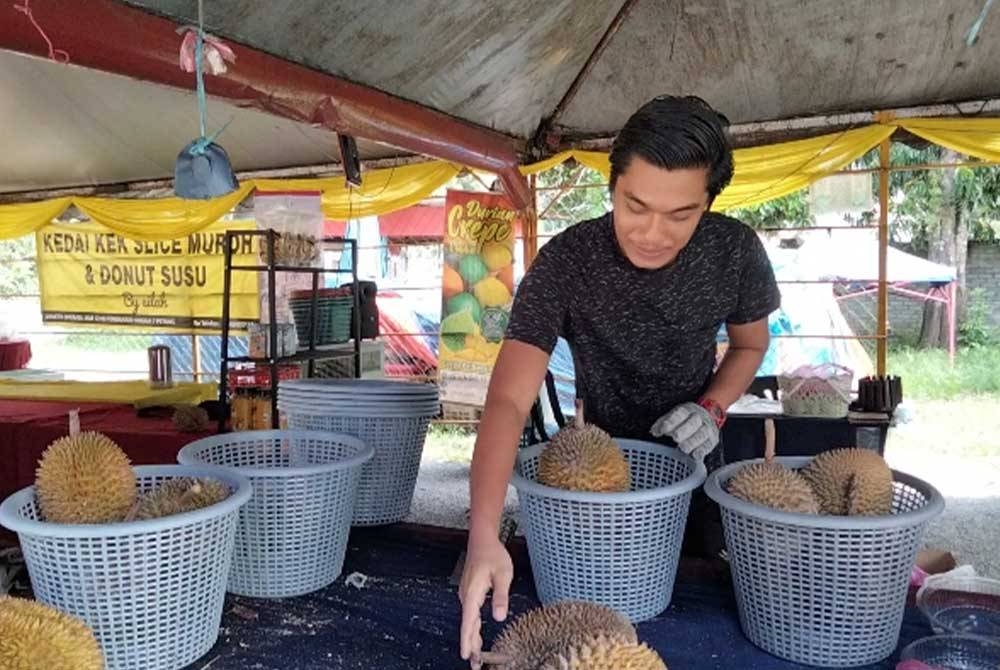 Nazrul Hisyam memasukkan durian ke dalam bakul sebelum dijual di gerainya di Jalan Pasir Tumbuh-Seribong pada Rabu.