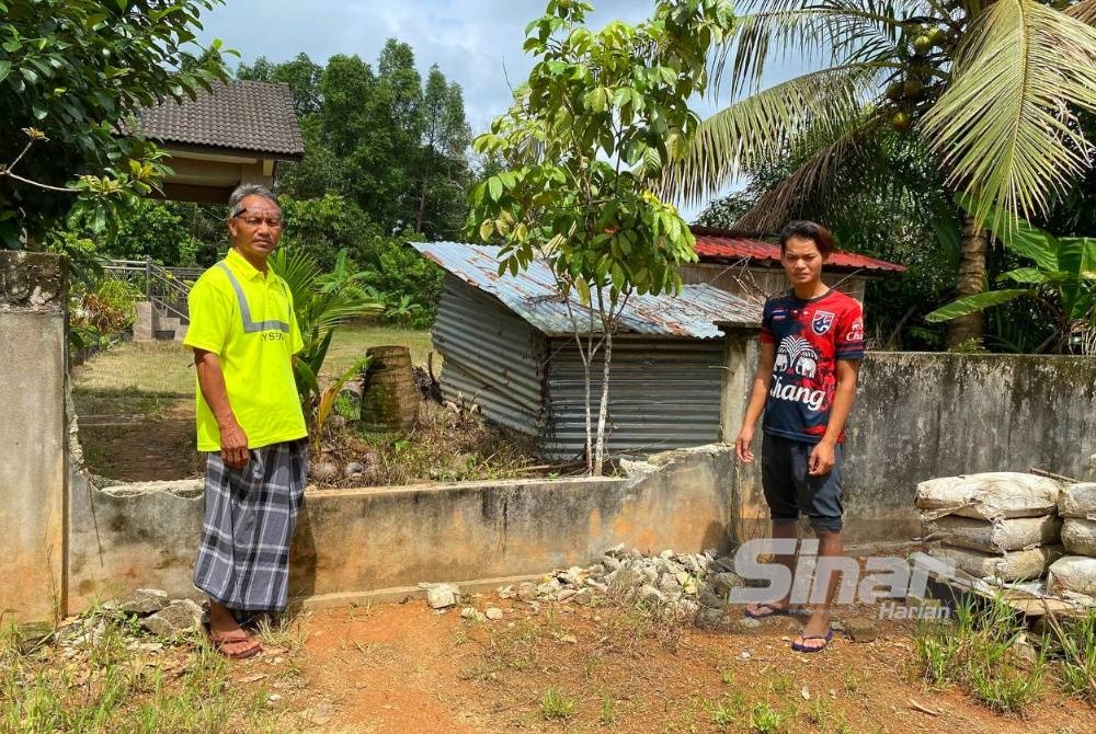 Wan Mohd Zain (kiri) menunjukkan pagar rumah Cikgu Soupi yang diruntuhkan bagi memberi peluang kepada 69 mangsa banjir di Masjid Mukim Padang Licin untuk menggunakan tandas di rumahnya.