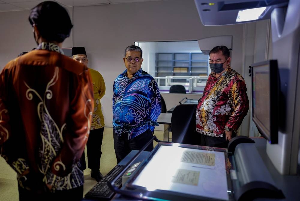 Aaron Ago melihat dari dekat proses pendigitalan rekod-rekod lama yang menggunakan alat pengimbas berteknologi tinggi ketika lawatan beliau ke Arkib Negara di Wisma Warisan, pada Khamis. - Foto Bernama